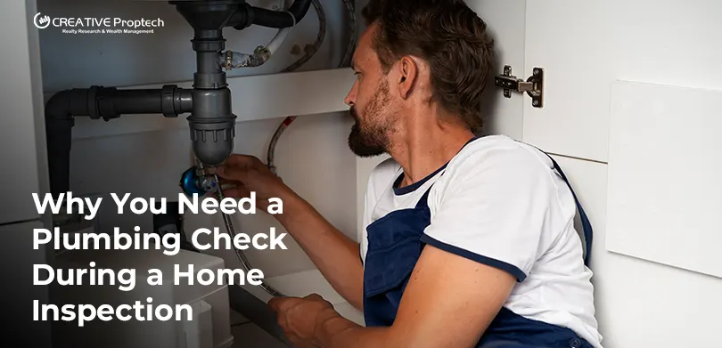 Male plumber in overalls inspecting pipes under a kitchen sink cabinet; text overlay reads 'Why You Need a Plumbing Check During a Home Inspection' with CREATIVE Proptech logo.