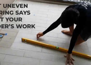 An inspector kneeling on a tiled balcony floor, using a spirit level to check for flatness and unevenness, illustrating the topic: What Uneven Flooring Says About Your Builder's Work.