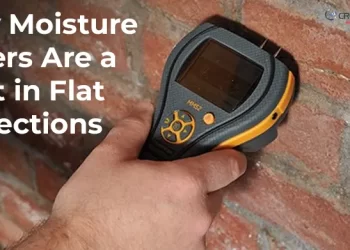 Close-up shot of a hand holding a moisture meter against a red brick wall, emphasizing why the tool is a must-have for flat inspections to detect hidden water damage and seepage.